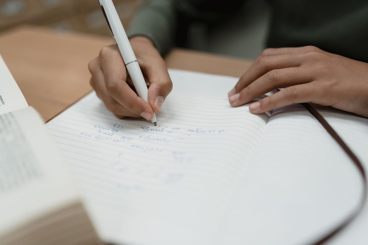 Mà escrivint un text a mà en una llibreta oberta